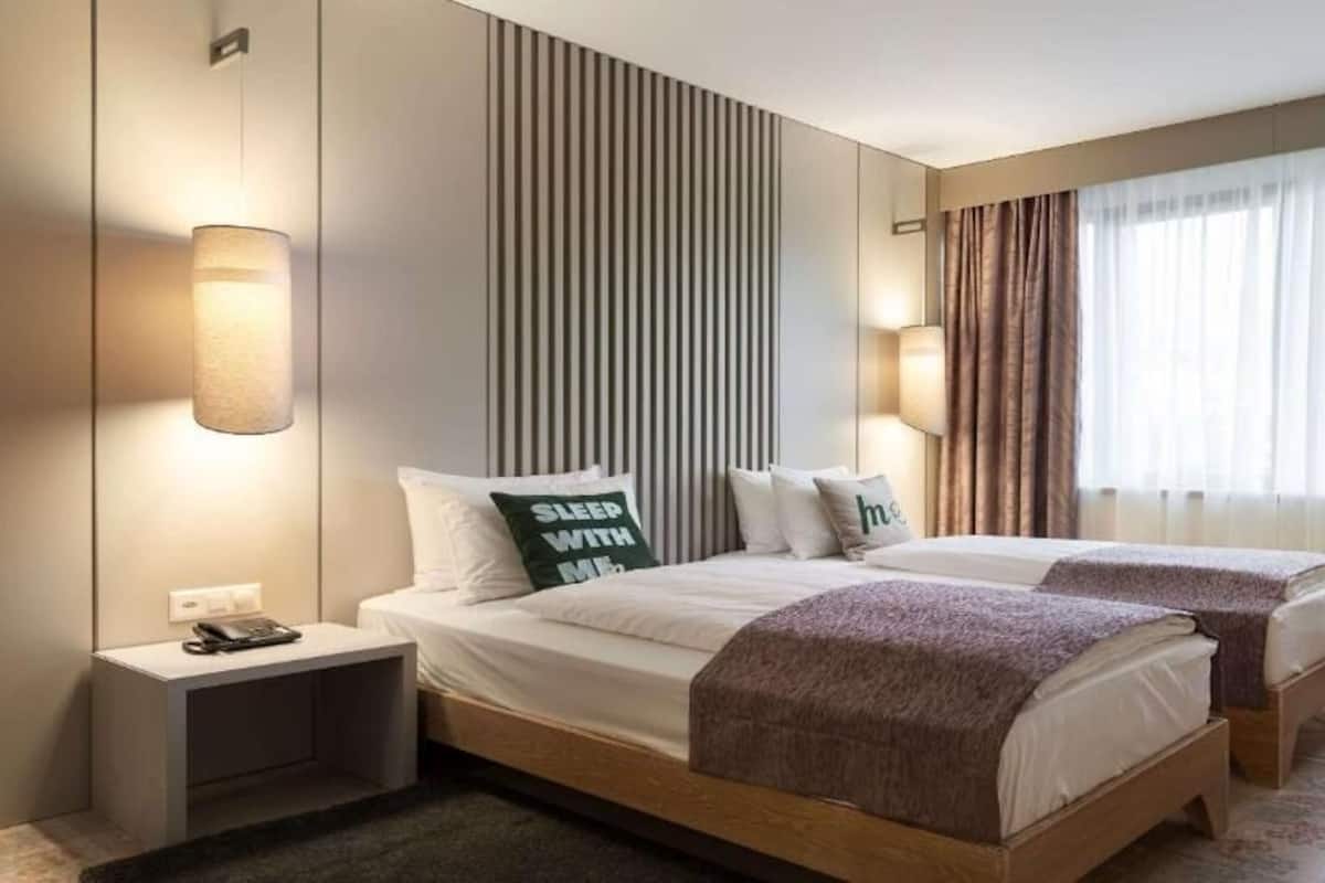 A double bed with two pillows, a bedside table with a phone, and a wall-mounted light fixture.