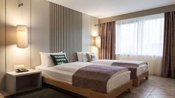 Una cama doble con dos almohadas, una mesita de noche con teléfono y una lámpara de pared.