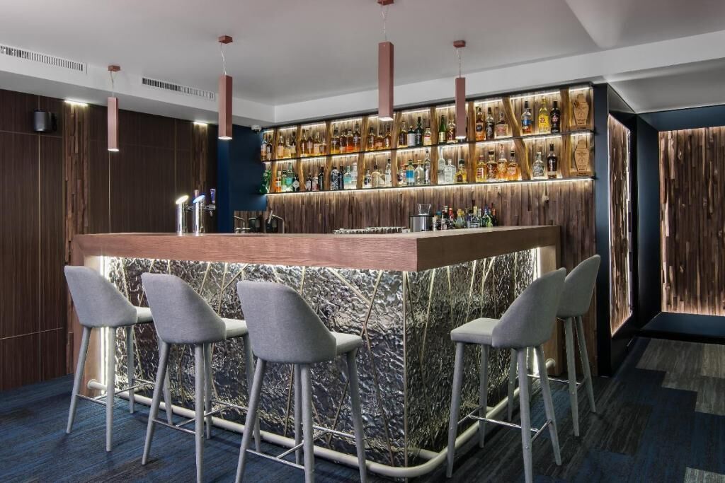 A bar area with a marble countertop, bar stools, and a variety of liquor bottles.