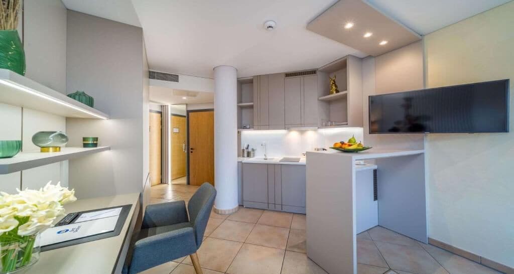 A modern kitchen with white cabinets, a dining area with a table and chairs, and a flat-screen TV mounted on the wall.