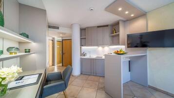A modern kitchen with white cabinets, a dining area with a table and chairs, and a flat-screen TV mounted on the wall.
