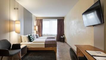 A hotel room with a bed, a desk, a chair, a TV, and a window with curtains.