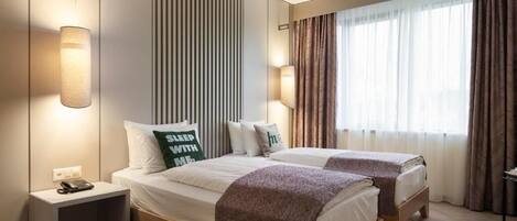 A hotel room with two beds, a bedside table with a phone, and a window with curtains.