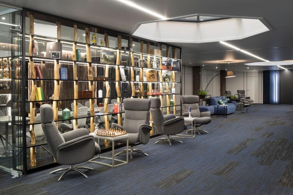 A modern lounge area with a glass wall displaying various items, comfortable seating, and a large ceiling light fixture.