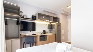 A compact hotel room with a kitchenette, a bed with white linens, and a chair. - Raízes Tatuapé (São Paulo)