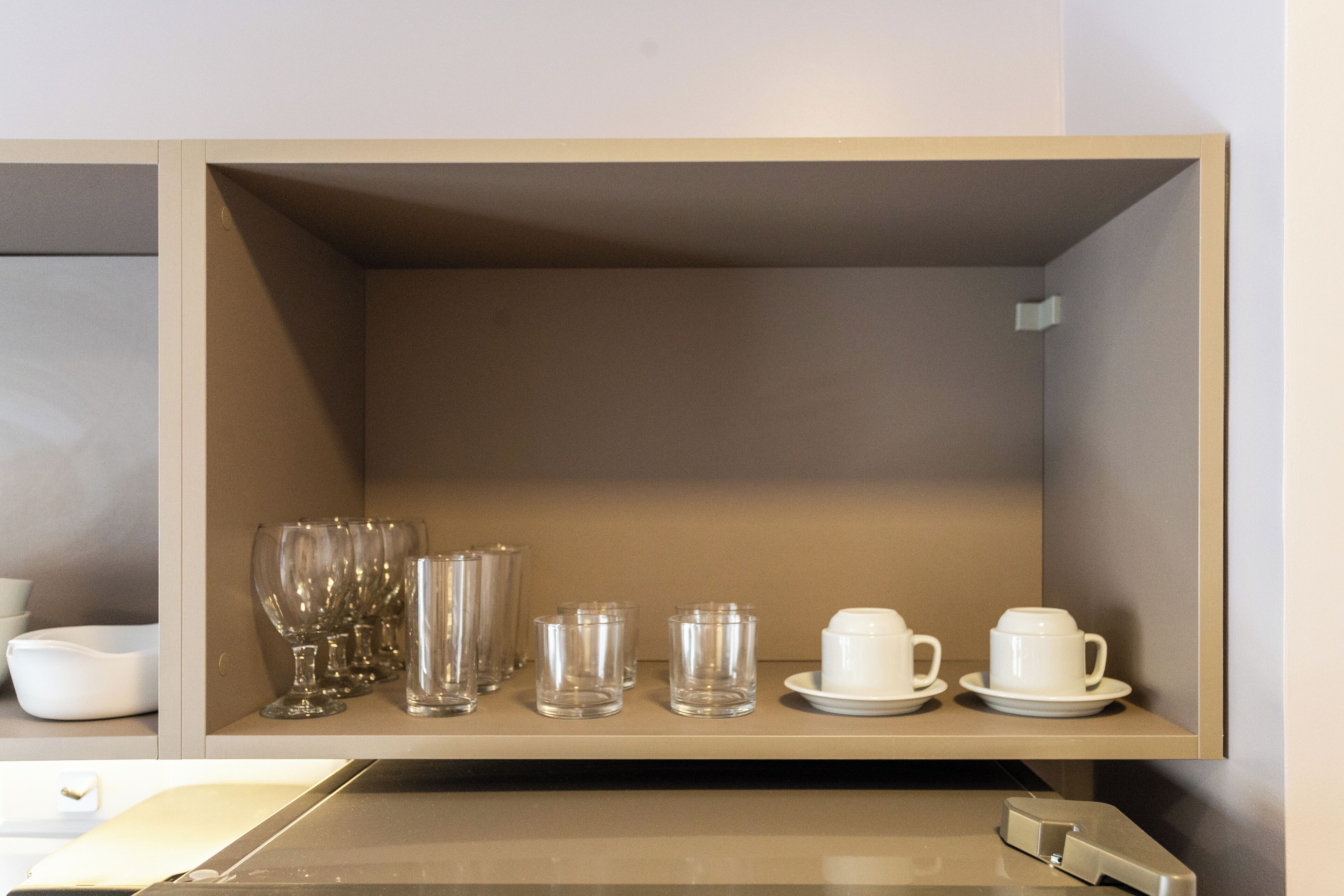 A shelf with various glassware and white ceramic cups and saucers.
