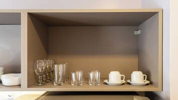 A shelf with various glassware and white ceramic cups and saucers.