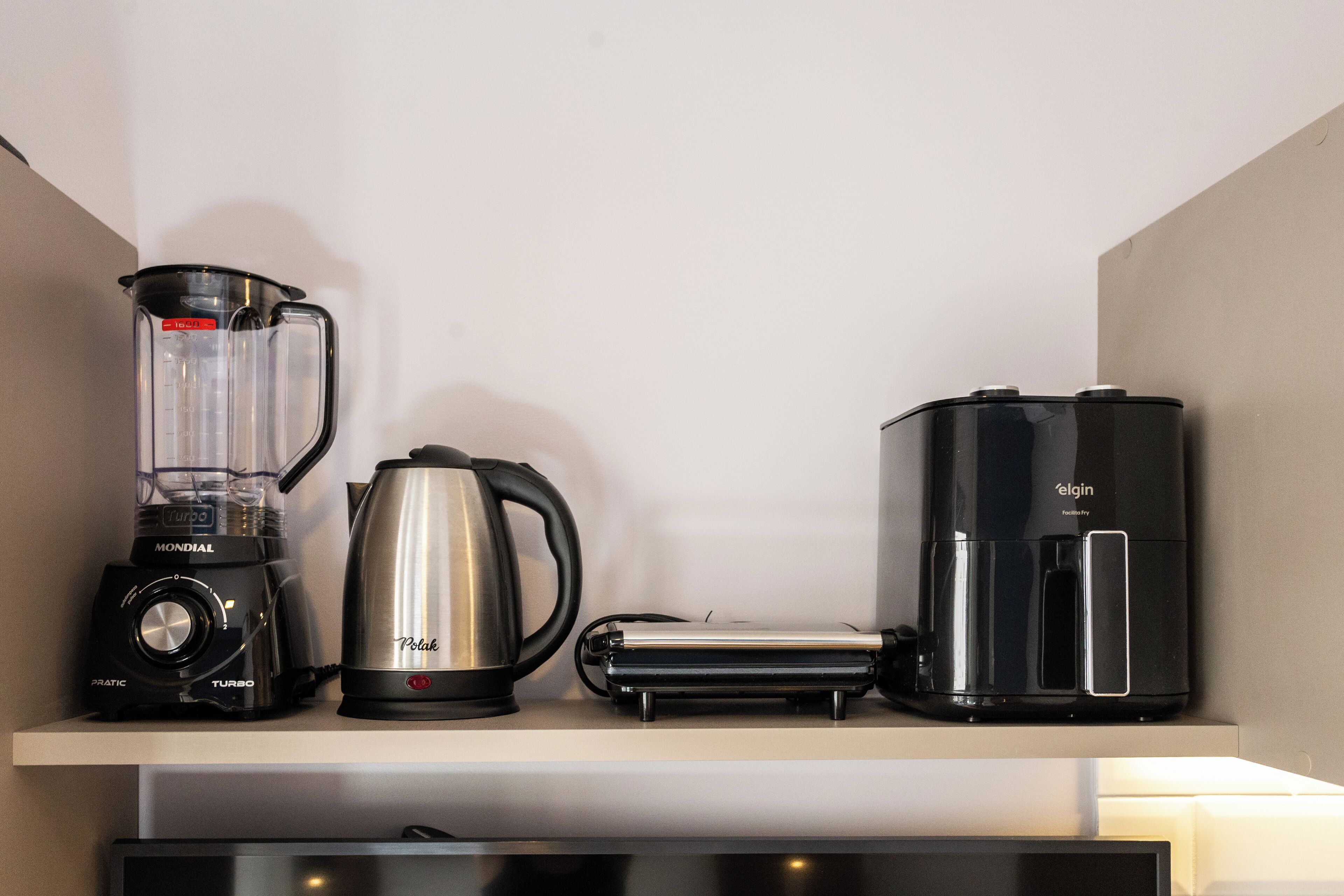 A kitchen counter with a blender, a kettle, a toaster, and a coffee maker.