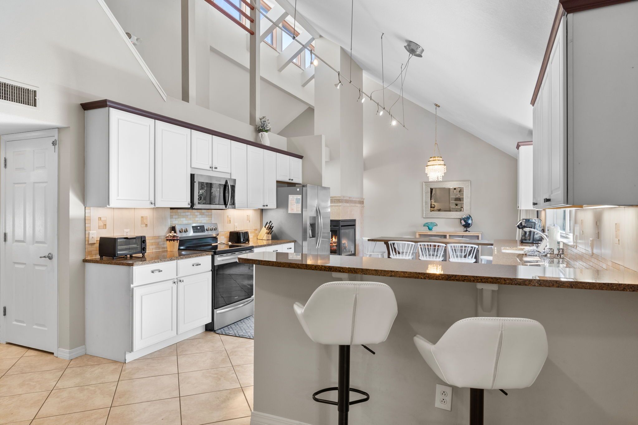 A modern kitchen with white cabinetry, a central island with bar stools, and a large window providing natural light.