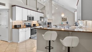 Een moderne keuken met witte kastjes, een centraal eiland met barstoelen en een groot raam voor natuurlijk licht.