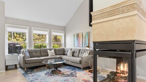 Een moderne woonkamer met een hoekbank, een glazen salontafel en een open haard.
