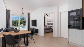 Ein modernes Hotelzimmer mit Essbereich, einer Küche, einem Schlafzimmer und Blick auf einen Swimmingpool.