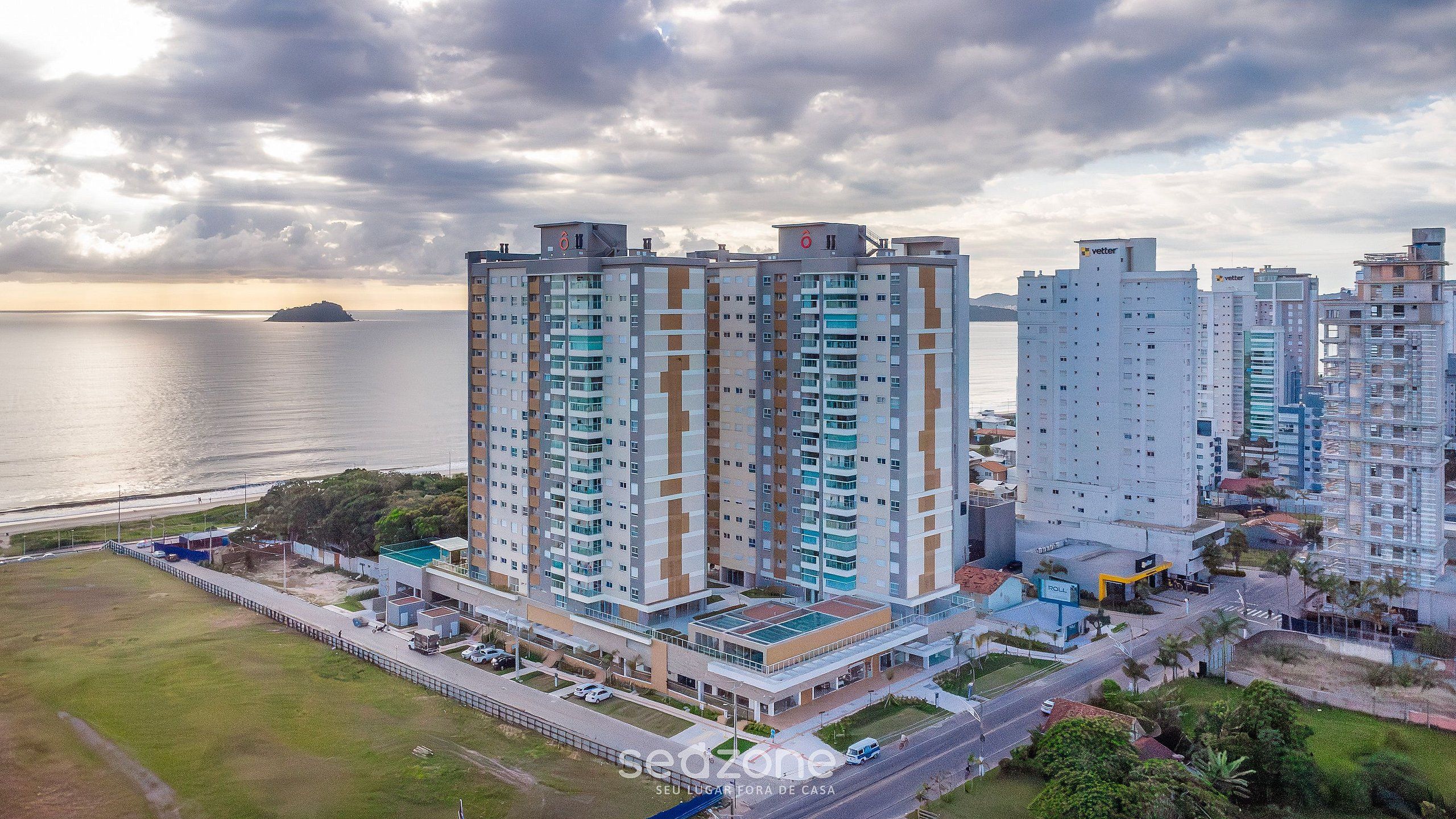 Un edificio residencial alto con varios balcones, un estacionamiento y vistas al mar.