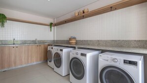 A laundry area with two front-loading washing machines, a wooden countertop, and a tiled backsplash. - Cond. c/ Academia a apenas 200 m da Praia de Piçarras - PTCs (Picarras)