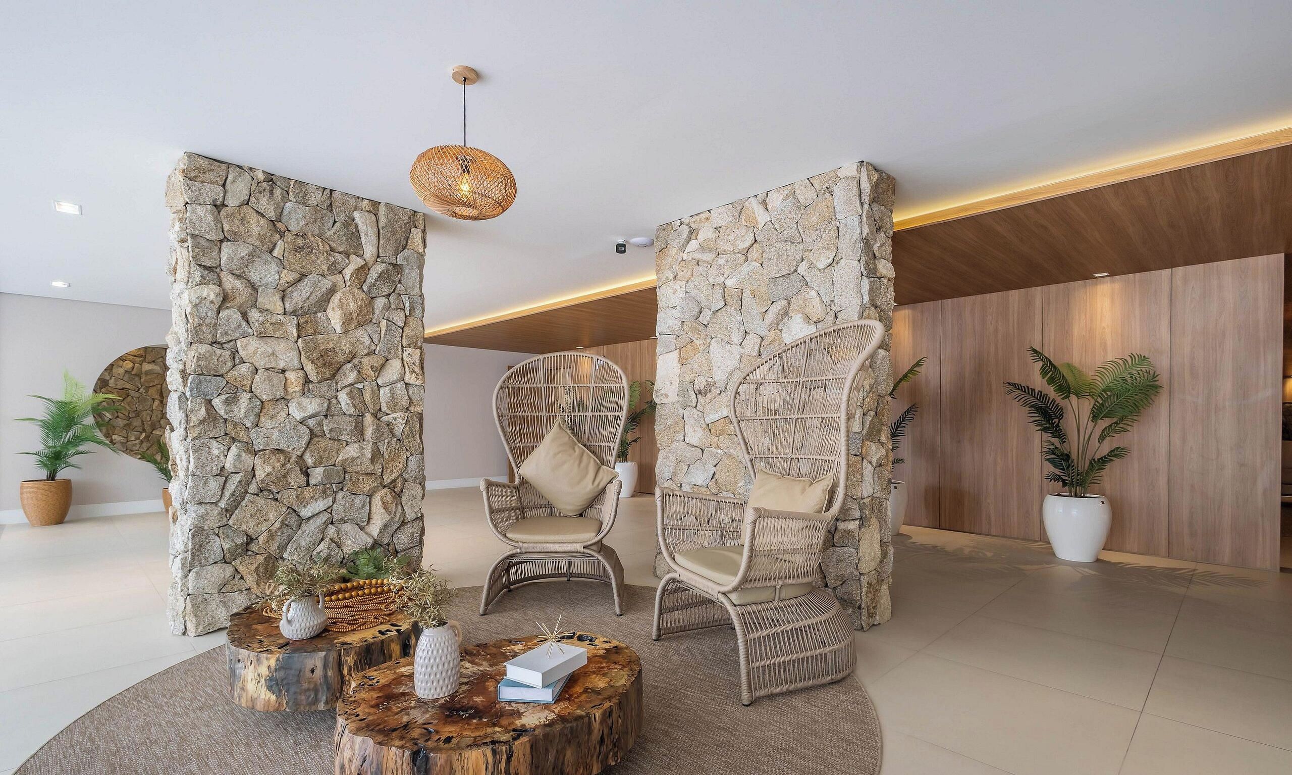 Un hall d’entrée moderne avec des murs en pierre, des fauteuils en osier et une table basse en bois.