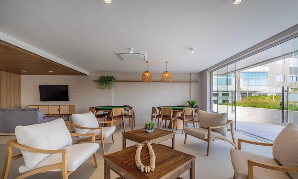 Una sala de estar moderna con mesa de billar, asientos cómodos, televisor de pantalla plana y grandes ventanas que ofrecen vistas a la ciudad.