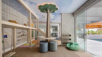 A modern playroom with a tree-shaped ceiling light, a slide, and a view of the outside.