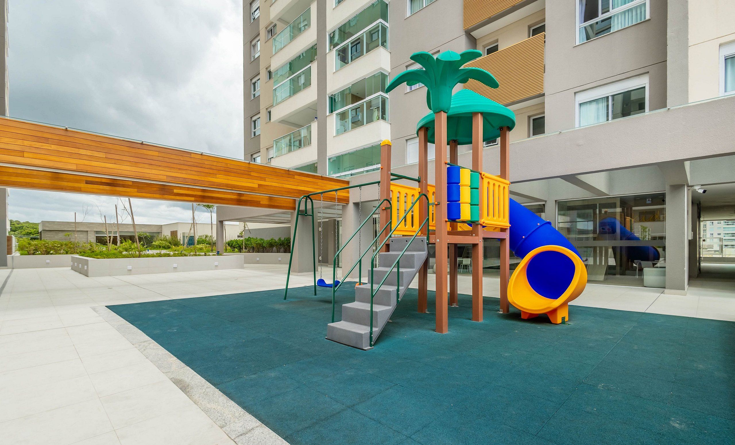 A playground with a slide and climbing structures, surrounded by a covered area and a building in the background.