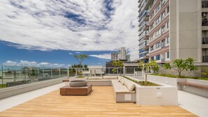 A rooftop terrace with a wooden floor, outdoor seating, and a view of the city skyline. - Cond. c/ Academia a apenas 200 m da Praia de Piçarras - PTCs (Picarras)