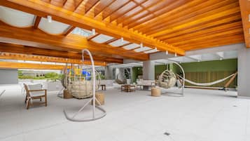 A spacious outdoor area with wooden ceiling beams, hanging chairs, and a hammock.