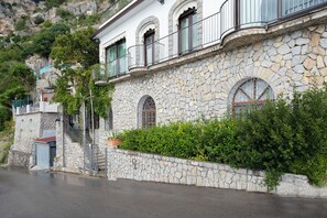 Um edifício de pedra com varandas, uma escadaria e um conjunto de sebe verdejante.
