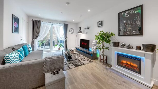 Un salon moderne avec un canapé gris, un téléviseur à écran plat, une cheminée et un tableau représentant un paysage urbain.
