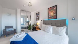 Une chambre d’hôtel moderne avec un grand lit, un canapé gris, un bureau avec une lampe et un miroir.