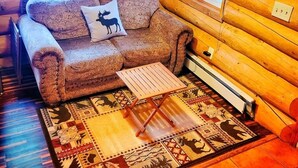 A cozy log cabin interior with a patterned sofa, a decorative pillow, a small wooden table, and a colorful rug. - ^^LOG CABIN ON THE RIVER! Alaskan Aurora Adventure (Fairbanks)