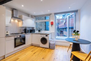 A modern kitchen with a built-in washing machine, a stove, and a large window offering a view of the city. - 4-Flat Entire Building | Sleeps 18 | Elizabeth Line to Heathrow | Farringdon (London)