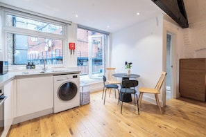 A compact kitchen with a washing machine, a sink, and a window overlooking a brick building. - 4-Flat Entire Building | Sleeps 18 | Elizabeth Line to Heathrow | Farringdon (London)