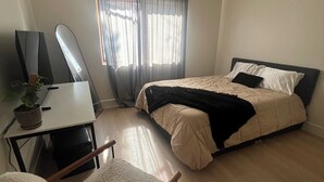 A bedroom with a bed, a desk, a chair, a TV, and a window with curtains. - Entire home 3bed w/ Laundry & 2 Spa like baths & private parking w/ EV charging (Long Beach)
