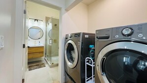 A laundry room with two washing machines, a dryer, and a small shelf with a bottle. - Entire home 3bed w/ Laundry & 2 Spa like baths & private parking w/ EV charging (Long Beach)