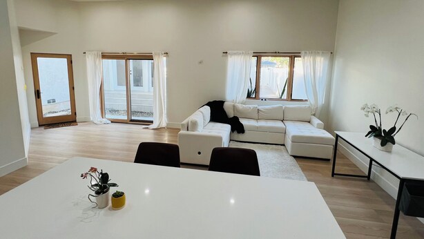A spacious living area with a white sofa, a dining table with chairs, and a small table with a plant. - Entire home 3bed w/ Laundry & 2 Spa like baths & private parking w/ EV charging (Long Beach)