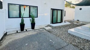 A modern building with a white exterior, two large windows, and a covered outdoor area with gravel and steps. - Entire home 3bed w/ Laundry & 2 Spa like baths & private parking w/ EV charging (Long Beach)