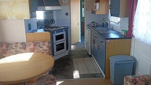 A compact kitchen with a stove, oven, sink, and cabinets. There is a dining table and a trash bin. - Atlas Moonstone (Skegness)