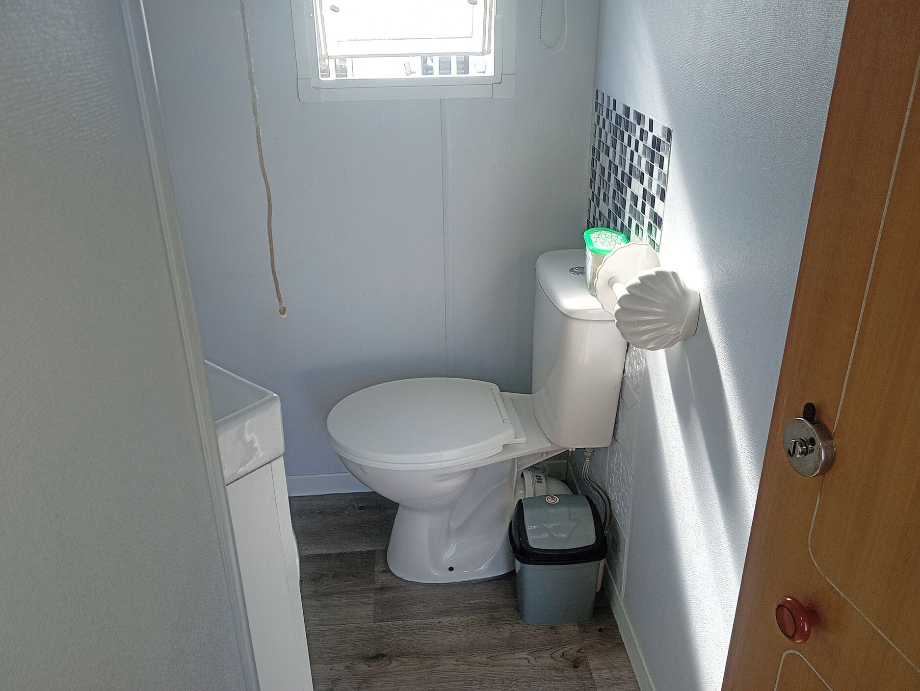 A small bathroom with a toilet, a trash bin, and a window.