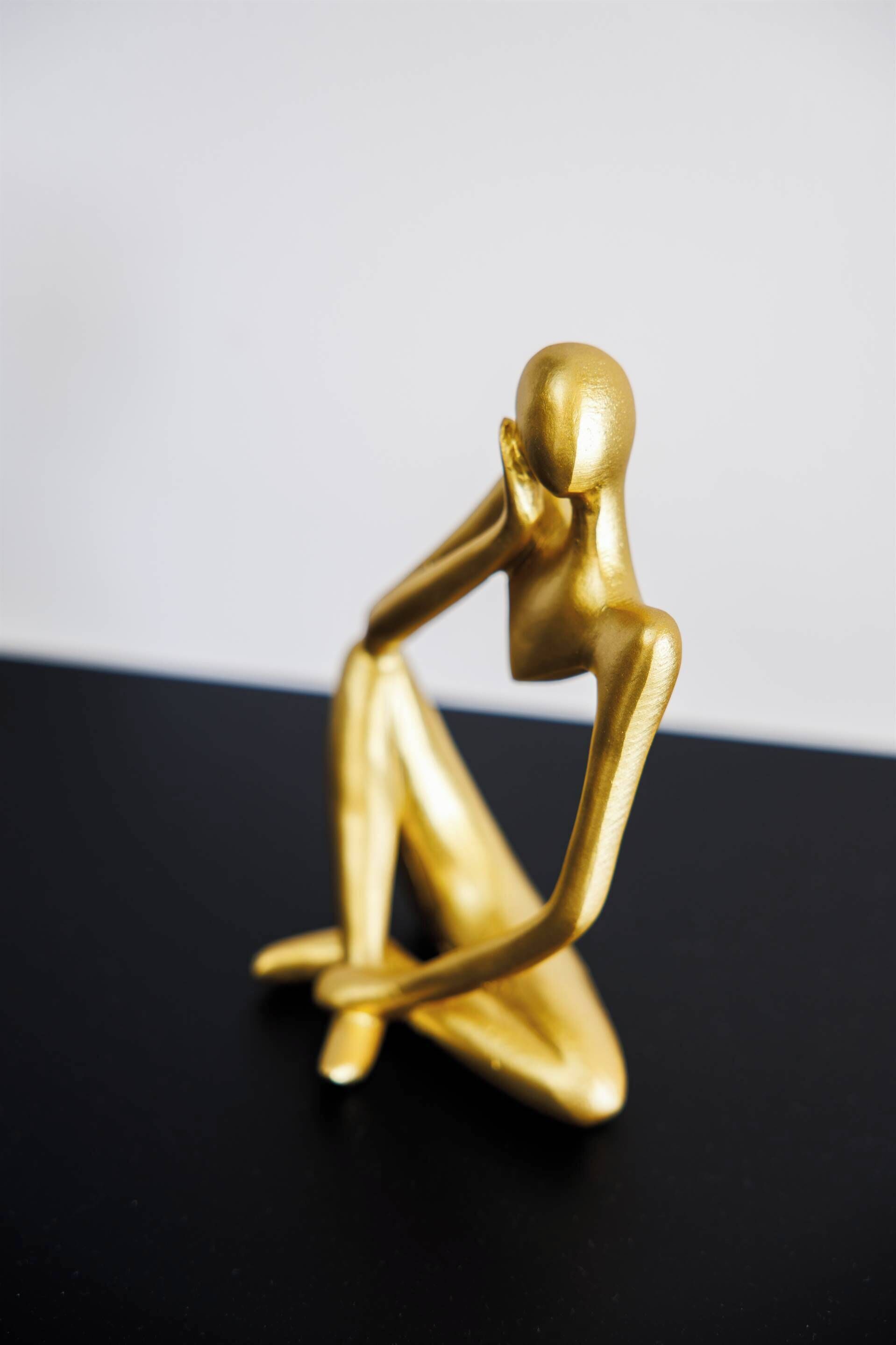 Een abstracte gouden sculptuur op een zwarte ondergrond.