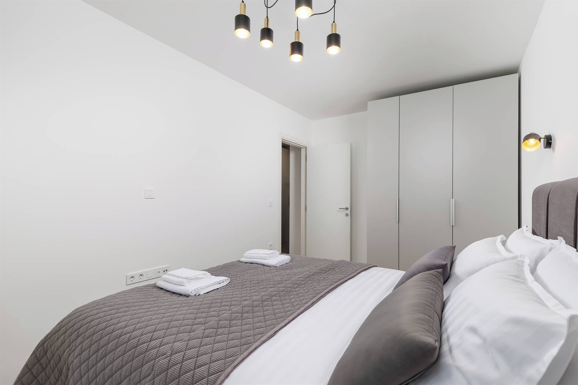 A modern bedroom with a bed, a wardrobe, and a ceiling light fixture.