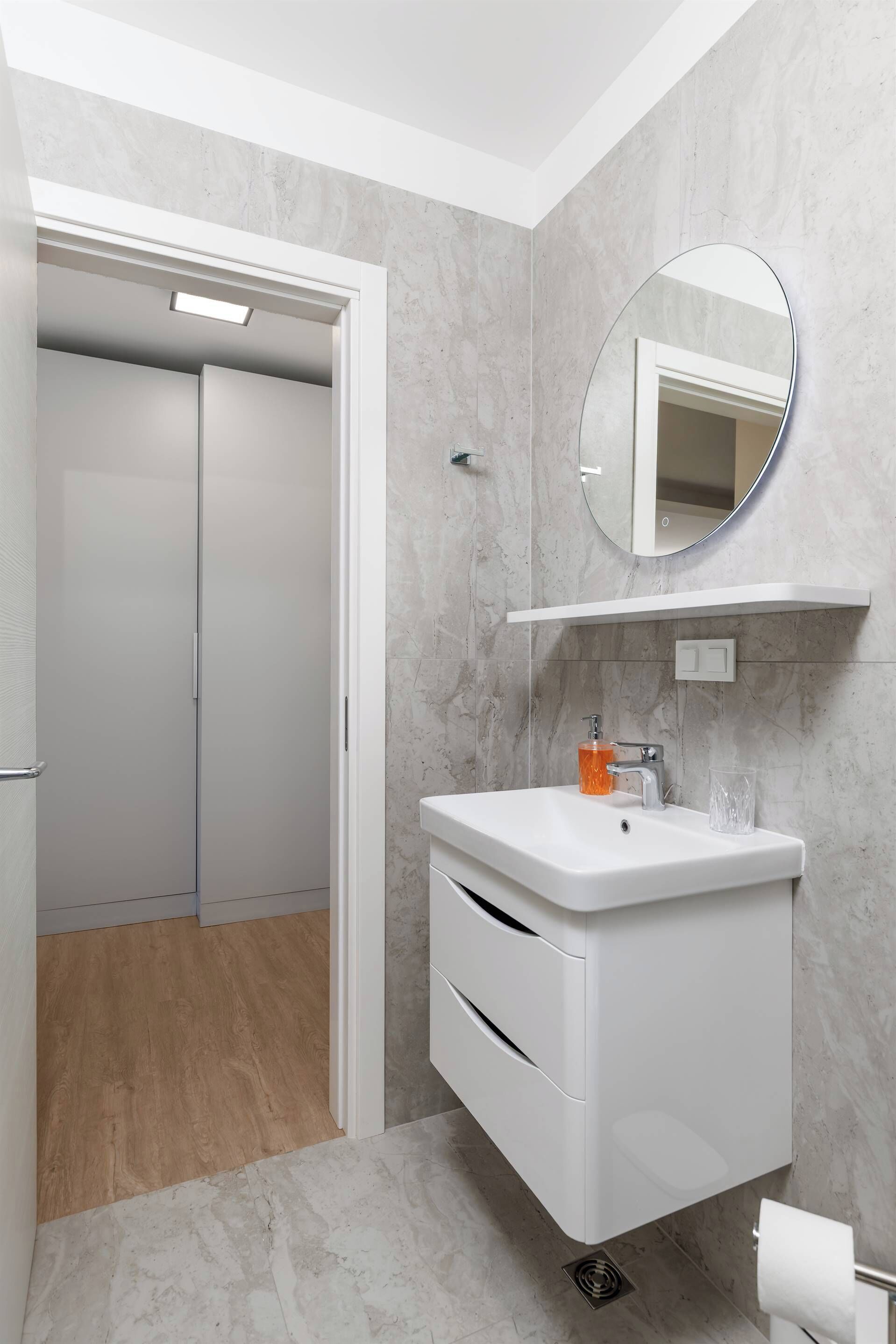 A modern bathroom with a white vanity, a round mirror, and a toilet paper holder.