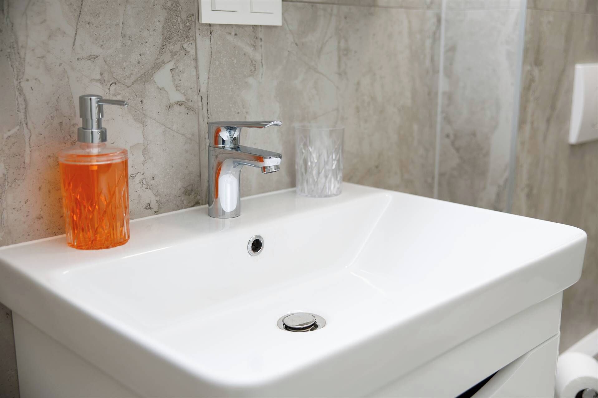 Un lavandino da bagno bianco con un rubinetto cromato e un erogatore di sapone.