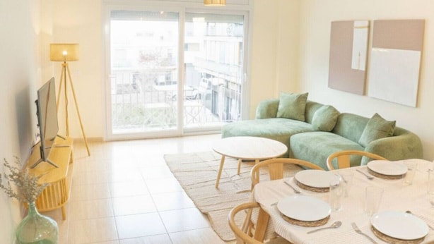 Una sala de estar moderna con un sofá verde, una mesa de comedor preparada para cuatro personas y un ventanal con vistas al exterior.