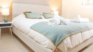 Una cama bien hecha con cabecera blanca, dos almohadas y una manta azul.
