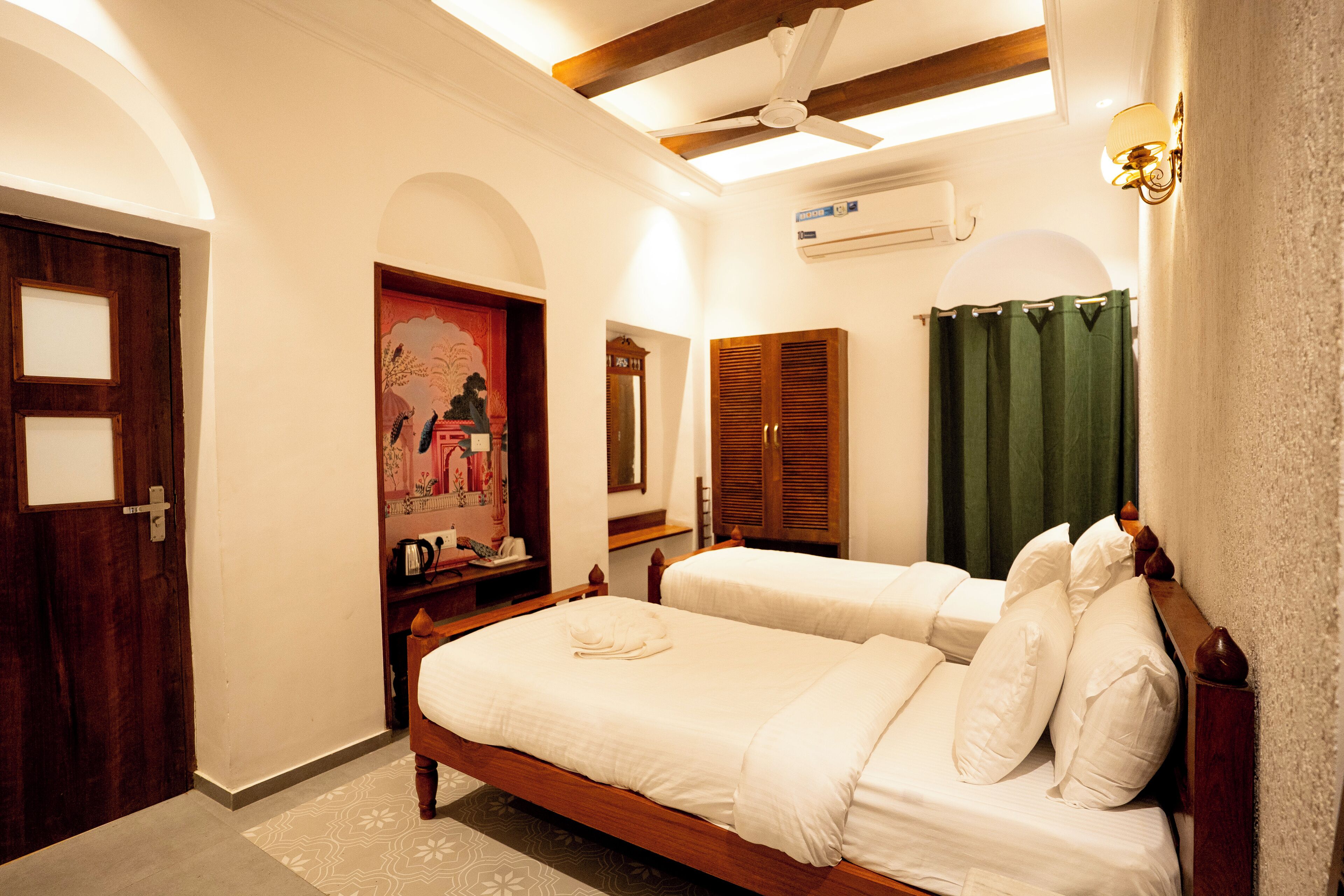 A bedroom with two single beds, a wooden wardrobe, a ceiling fan, and a painting on the wall.