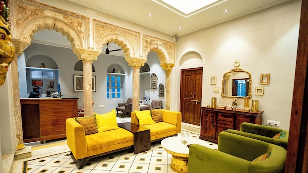 A traditional interior with a sofa set, a green armchair, a coffee table, and a wooden cabinet. - SHIVA KASHI HOTEL (Varanasi)