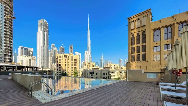 A rooftop pool with a city skyline view, including high-rise buildings and a distinctive tower. - StayShort - Downtown 2 Bed Unit with Burj Views that Sleeps 4 (Downtown)
