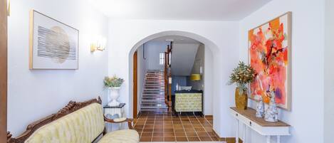 A hallway with a sofa, a console table with decorative items, and a staircase leading to a kitchen area.