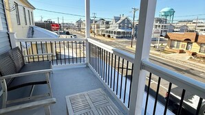 A covered balcony with a table and chairs, overlooking a street with houses and a water tower. - Beach Block heart of Downtown Walk to Everything (Sea Isle City)