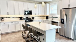 A modern kitchen with white cabinets, stainless steel appliances, and a central island with bar stools. - Beach Block heart of Downtown Walk to Everything (Sea Isle City)