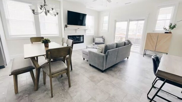 A spacious living room with a gray sofa, a dining table with chairs, a chandelier, and a ceiling fan. - Beach Block heart of Downtown Walk to Everything (Sea Isle City)