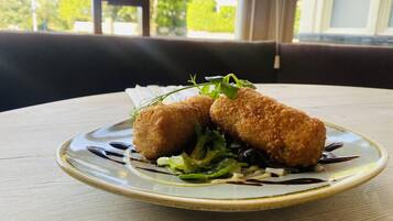 Un plato con dos croquetas doradas, ensalada verde y una salsa oscura sobre un plato de cerámica.